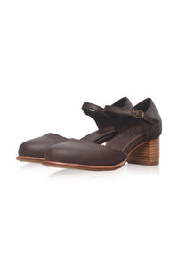 A pair of dark brown leather Mary Jane style shoes with a stacked wood-look block heel and a small gold buckle on the strap, shown on a white background.