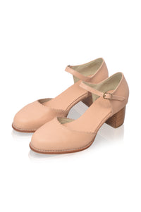 A pair of women's Mary Jane style shoes in a light peach-beige color, featuring a low block heel and a small gold buckle on the strap, shown on a white background.