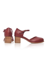 A pair of women's low block-heel sandals in a deep burgundy red leather, featuring a strap with a small bow on the side and a stacked wood-look heel, shown from both front and side angles against a white background.