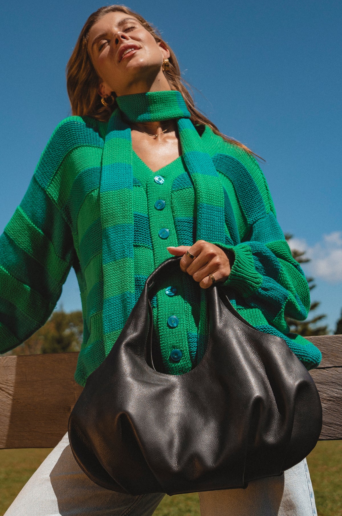 Woman wearing a green cardigan holding a black handbag outdoors.