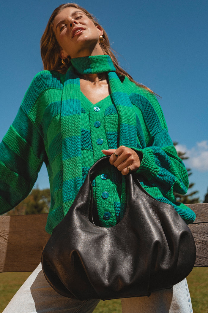 Woman wearing a green cardigan holding a black handbag outdoors.