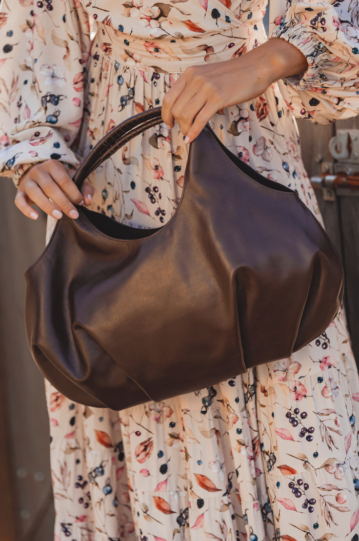 Person holding a brown leather handbag wearing a floral dress.
