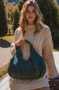 Woman holding a green bag outdoors with trees and grass in the background