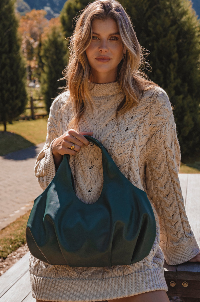 Woman holding a green bag outdoors with trees and grass in the background