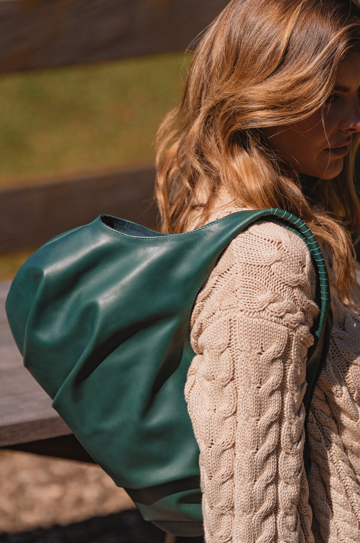 Person wearing a beige knitted sweater with a green bag over their shoulder outdoors.