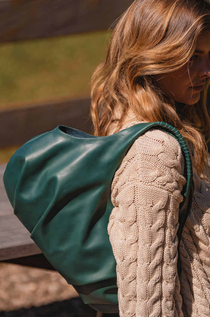 Person wearing a beige knitted sweater with a green bag over their shoulder outdoors.