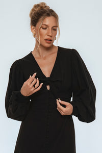 Woman wearing a black dress with a bow detail on a light gray background