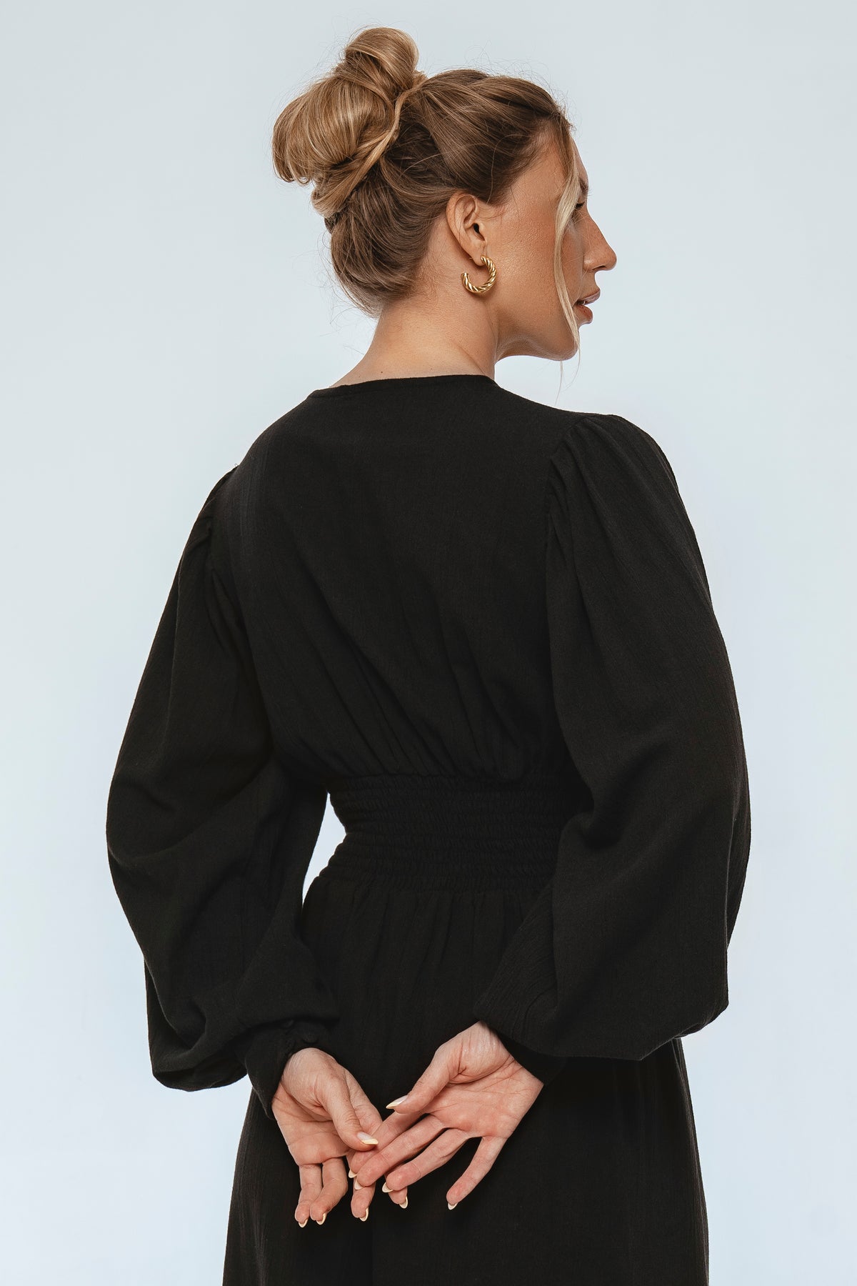 Woman wearing a black dress with long sleeves against a light gray background