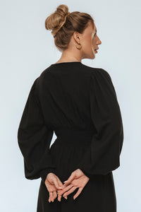 Woman wearing a black dress with long sleeves against a light gray background