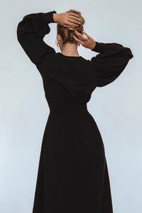 Person wearing a black dress with puffed sleeves against a light background