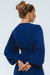 Woman wearing a blue dress with long sleeves on a light gray background