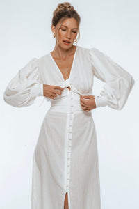 Woman wearing a white dress with long sleeves on a plain background