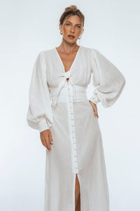 Woman wearing a white dress with long sleeves on a plain background