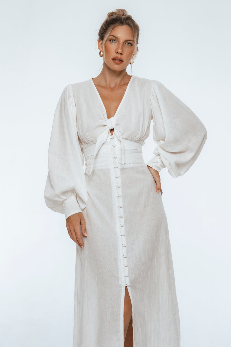 Woman wearing a white dress with long sleeves on a plain background