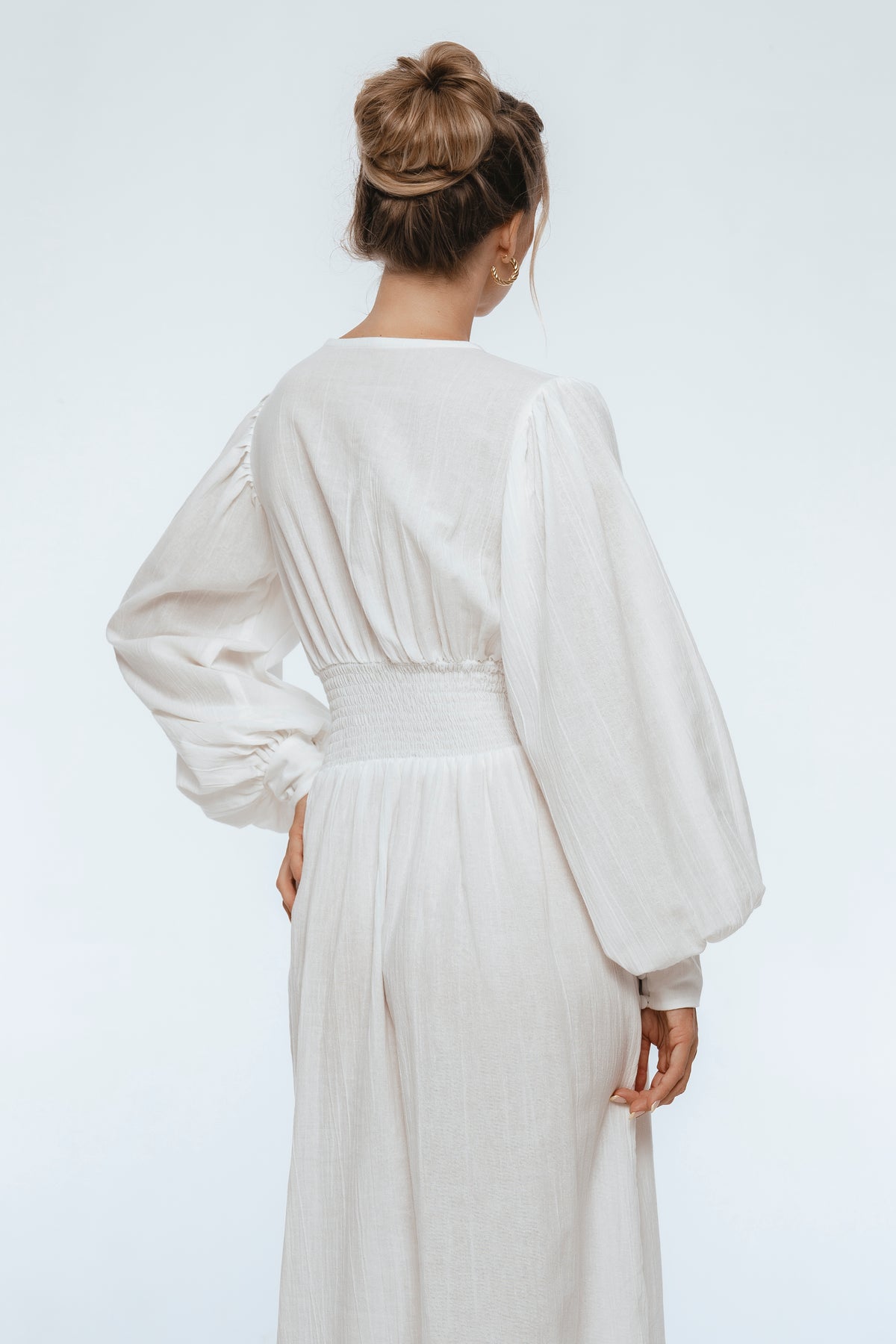 Person wearing a white outfit with long sleeves on a plain background