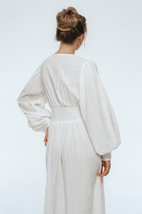 Person wearing a white outfit with long sleeves on a plain background