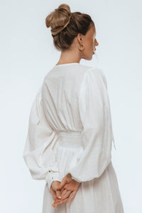 Woman wearing a white dress with long sleeves on a light gray background