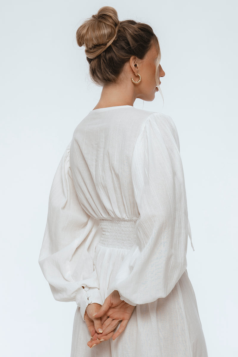 Woman wearing a white dress with long sleeves on a light gray background