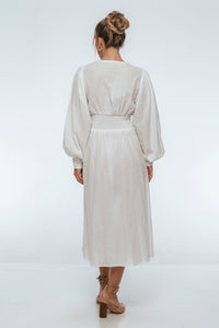 Woman wearing a long, light-colored dress with long sleeves on a white background