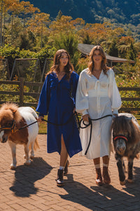 Two women walking with small ponies on a paved path with a scenic background