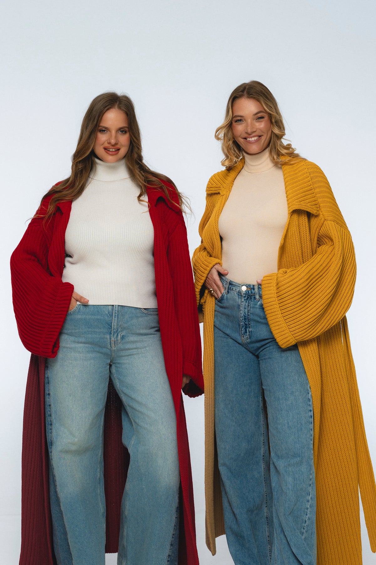 Two women wearing long cardigans and jeans on a white background