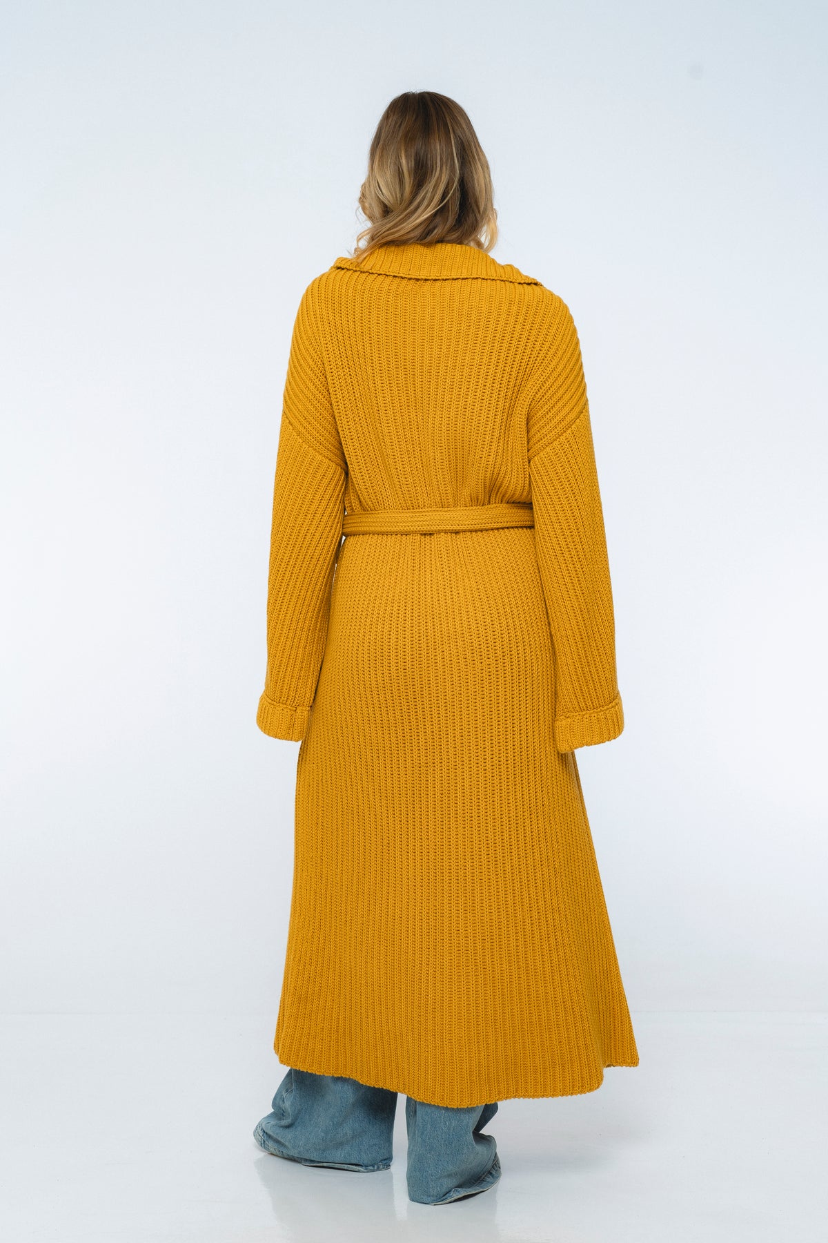 Person wearing a long yellow ribbed coat on a white background