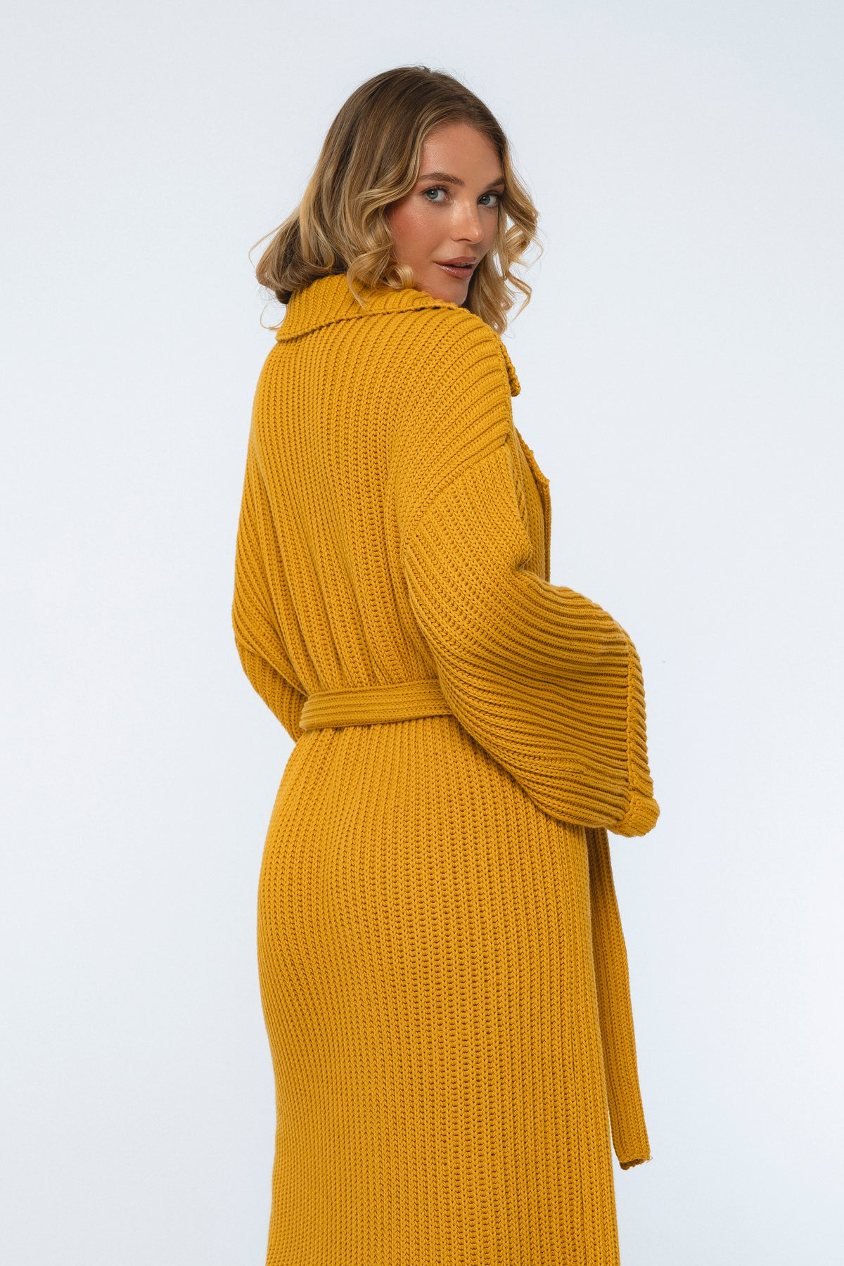Woman wearing a mustard yellow knitted coat on a white background