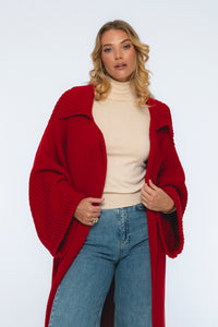 Woman wearing a red cardigan, beige turtleneck, and blue jeans on a white background