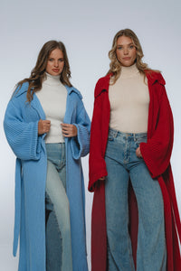 Two women wearing long cardigans, one blue and one red, standing side by side against a white background.