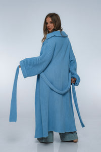 Woman wearing a long blue knitted coat on a white background