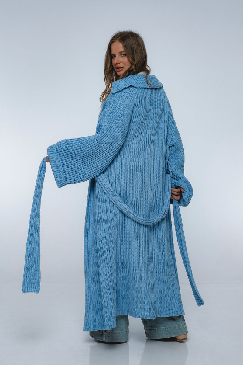 Woman wearing a long blue knitted coat on a white background