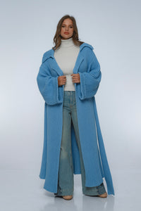 Woman wearing a long blue knitted coat on a white background