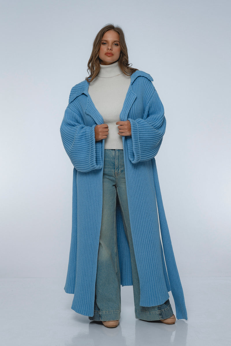 Woman wearing a long blue knitted coat on a white background