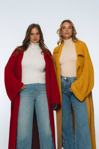 Two women wearing long coats and jeans on a white background