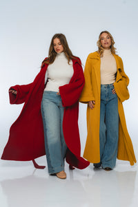 Two women wearing long coats, one red and one yellow, standing on a white background.
