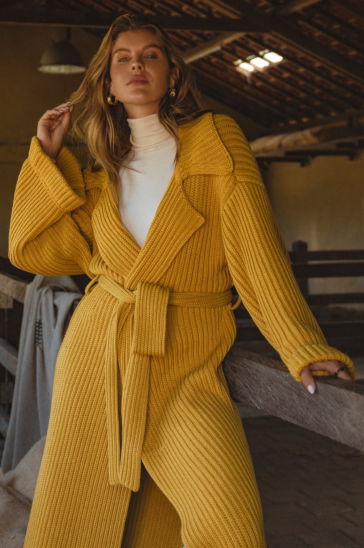Woman wearing a yellow knitted coat sitting on a wooden bench in the barn.