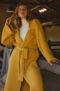 Woman wearing a yellow knitted coat sitting on a wooden bench in the barn.