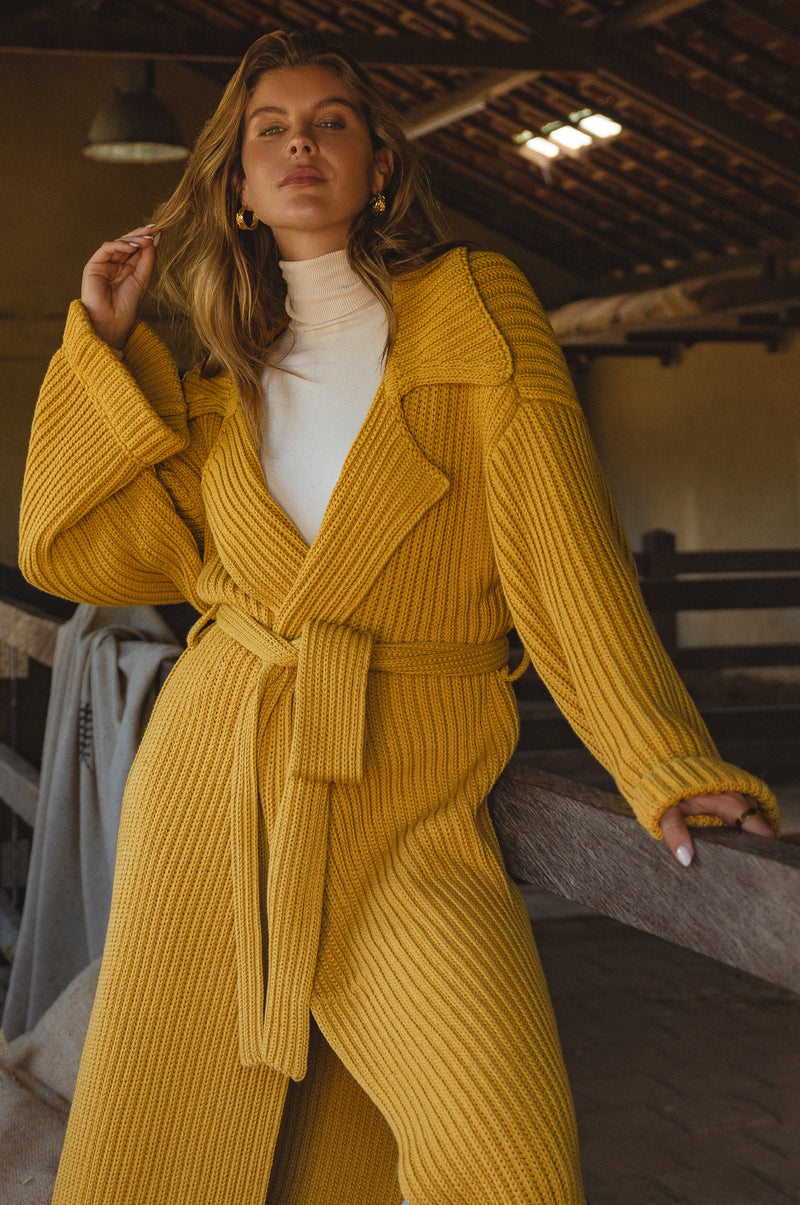 Woman wearing a yellow knitted coat sitting on a wooden bench in the barn.