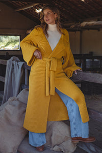 Woman wearing a yellow knitted coat sitting on a wooden bench in the barn.