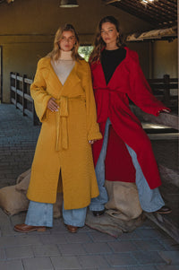Two women wearing long coats, one yellow and one red, standing in an outdoor setting.