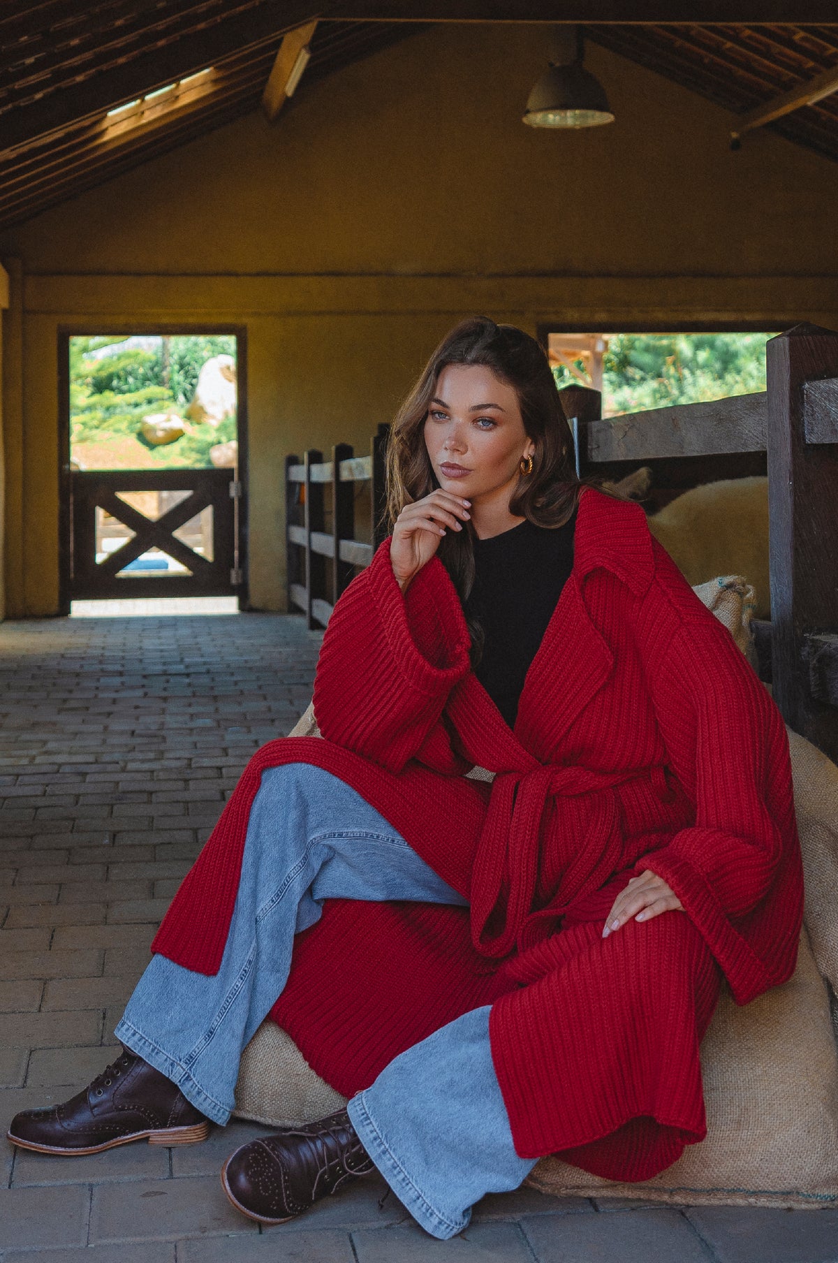 Woman wearing a red robe sitting in a barn-like setting