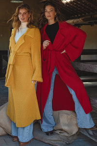 Two women wearing long, colorful coats standing indoors.