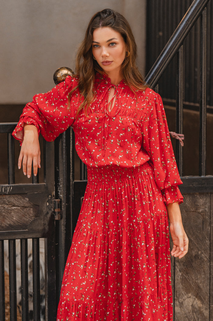 Woman wearing a red floral dress standing against a dark metal railing.